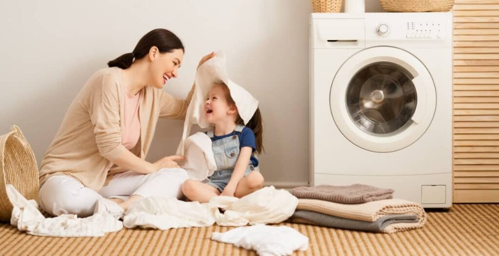 Beautiful young woman and child girl little helper are having fun and smiling while doing laundry at home