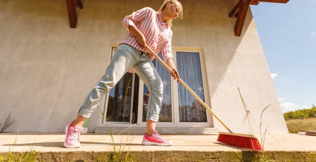 Female adult young woman using big broom to clean up backyard patio