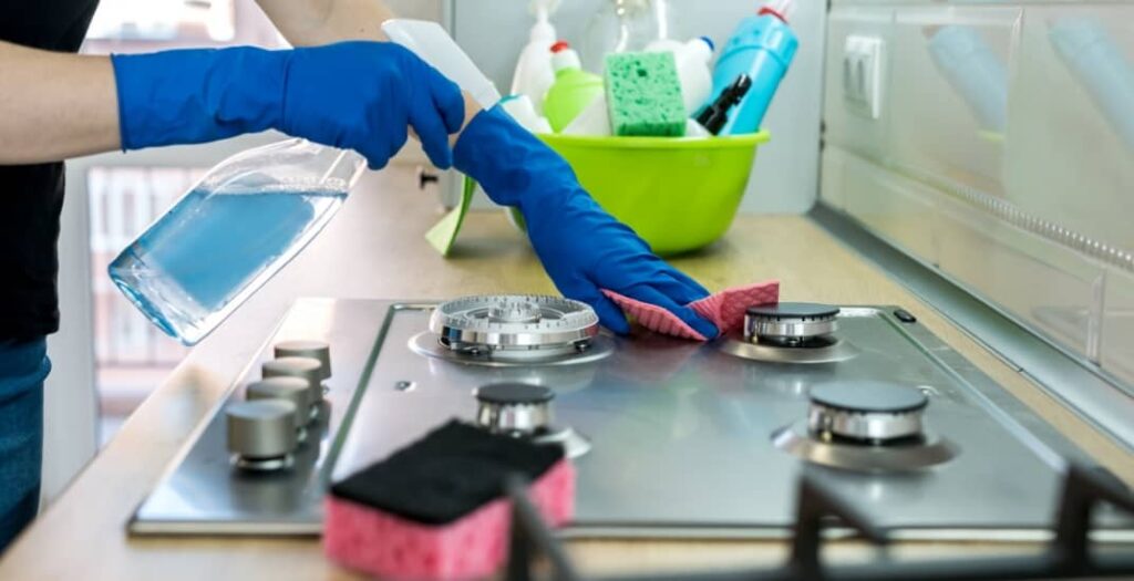Woman cleaning stainless steel gas surface in the kitchen with rubber gloves