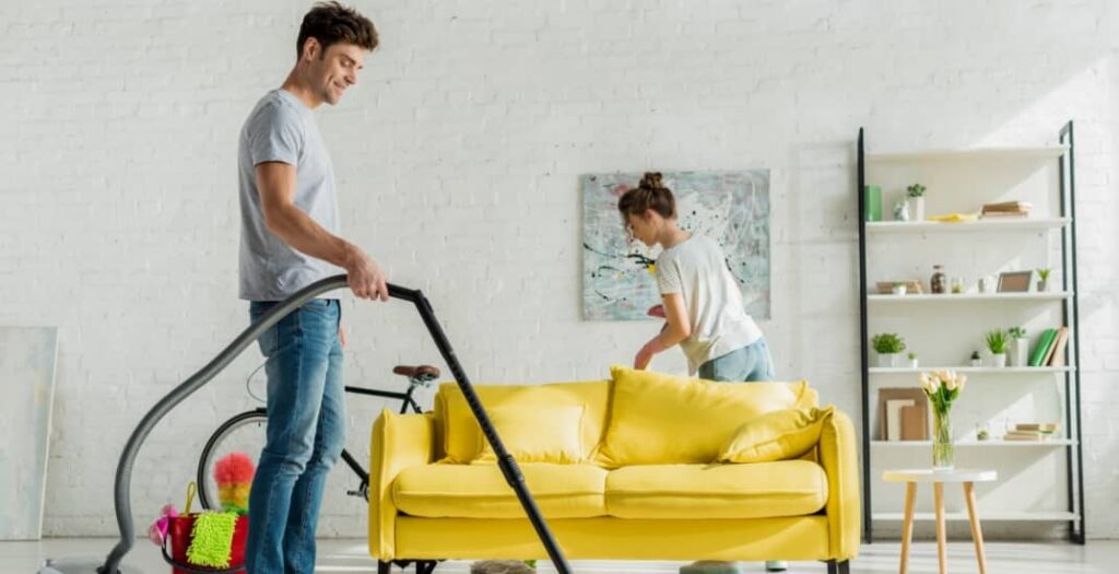 happy man using vacuum cleaner near woman in living room