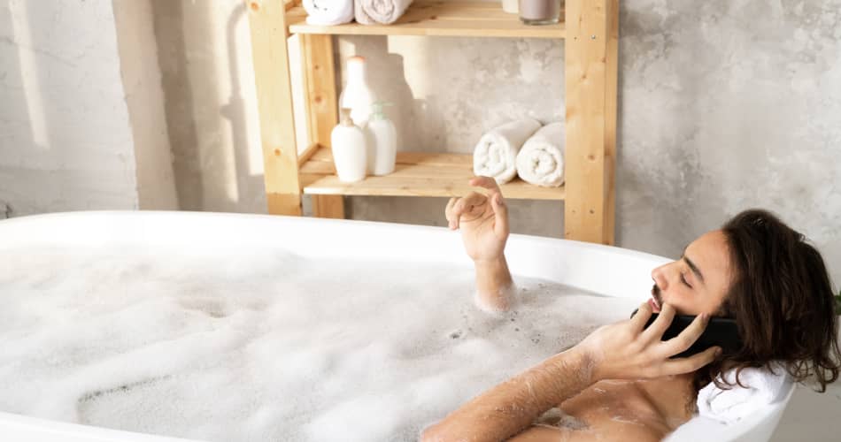 img - young-restful-man-talking-smartphone-while-lying-bathtub-filled-water